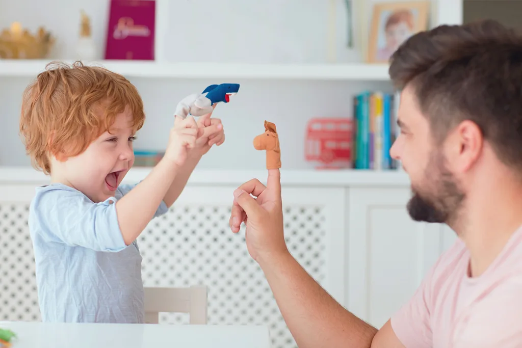 A young boy and his male au pair engage in imaginative play-based learning as they happily tell stories with finger puppets.