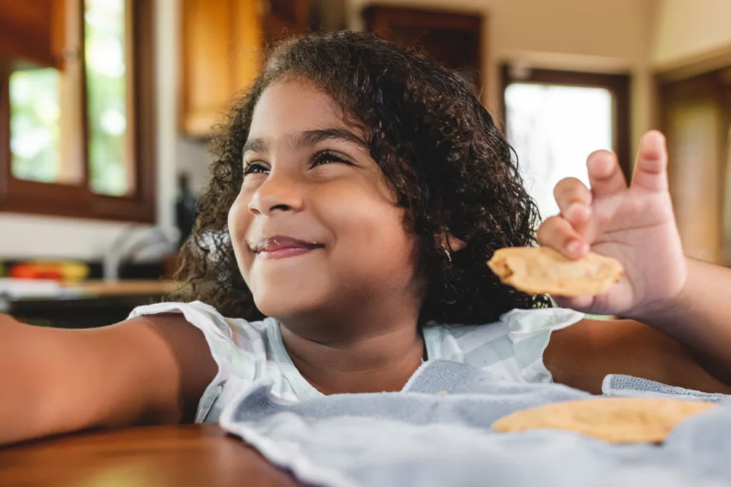 A young girl smiles brightly while holding an empanada, celebrating the culinary traditions of South American culture.