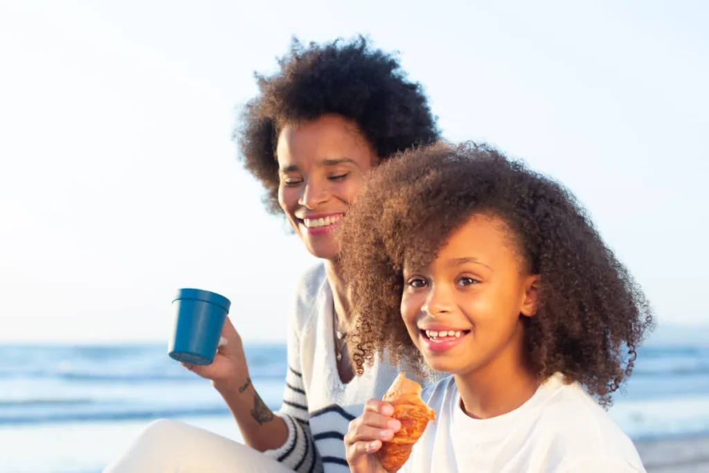 A woman smiles fondly while a young girl holds what appears to be a French pastry, maybe introducing French food for kids.