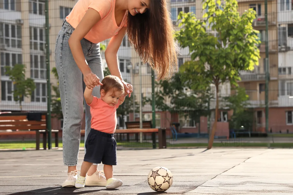 An au pair playing soccer with a young child in a park, fostering cultural exchange and bonding through shared activities.