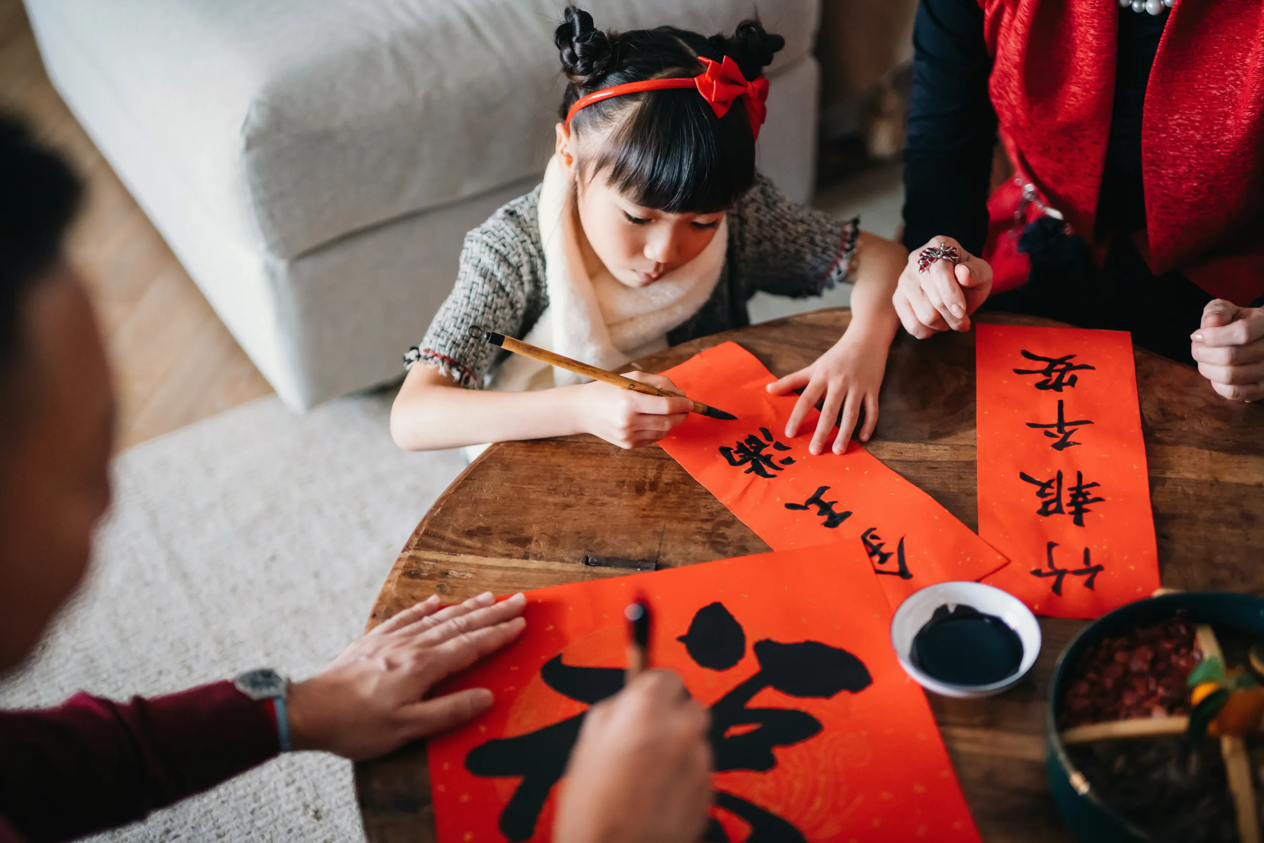 Grandparents practising Chinese calligraphy for Chinese New Year Fai Chun (Auspicious Messages) and teaching their granddaughter by writing it on couplets at home